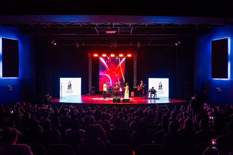 Auditório cheio numa apresentação da ASM, com a banda no palco e os telões da escola dos dois lados
