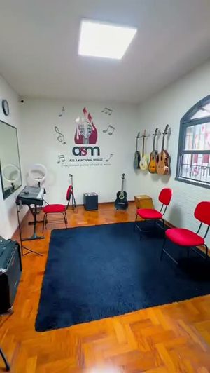 Sala de aula da ASM com tapete azul, cadeiras vermelhas, violões pendurados na parede e o logo da escola